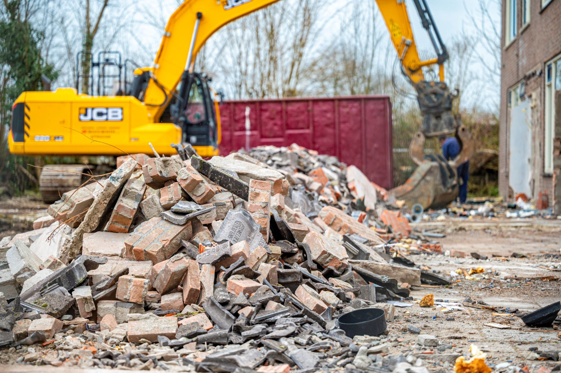 Bouwplaats met sloopafval en gele graafmachine.